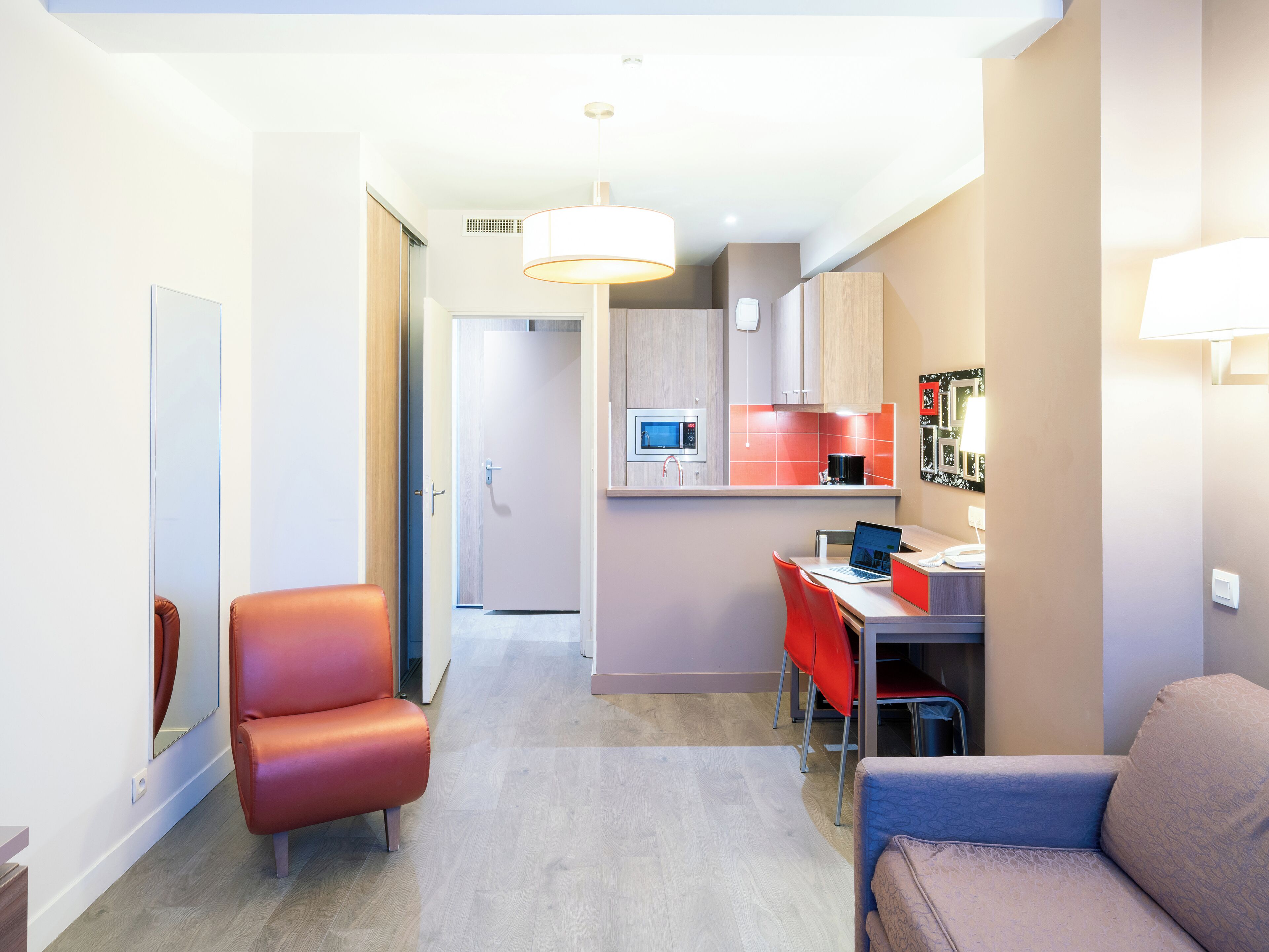 A modern kitchen with a microwave, stove, and red accents. There is a dining area with a laptop and chairs.