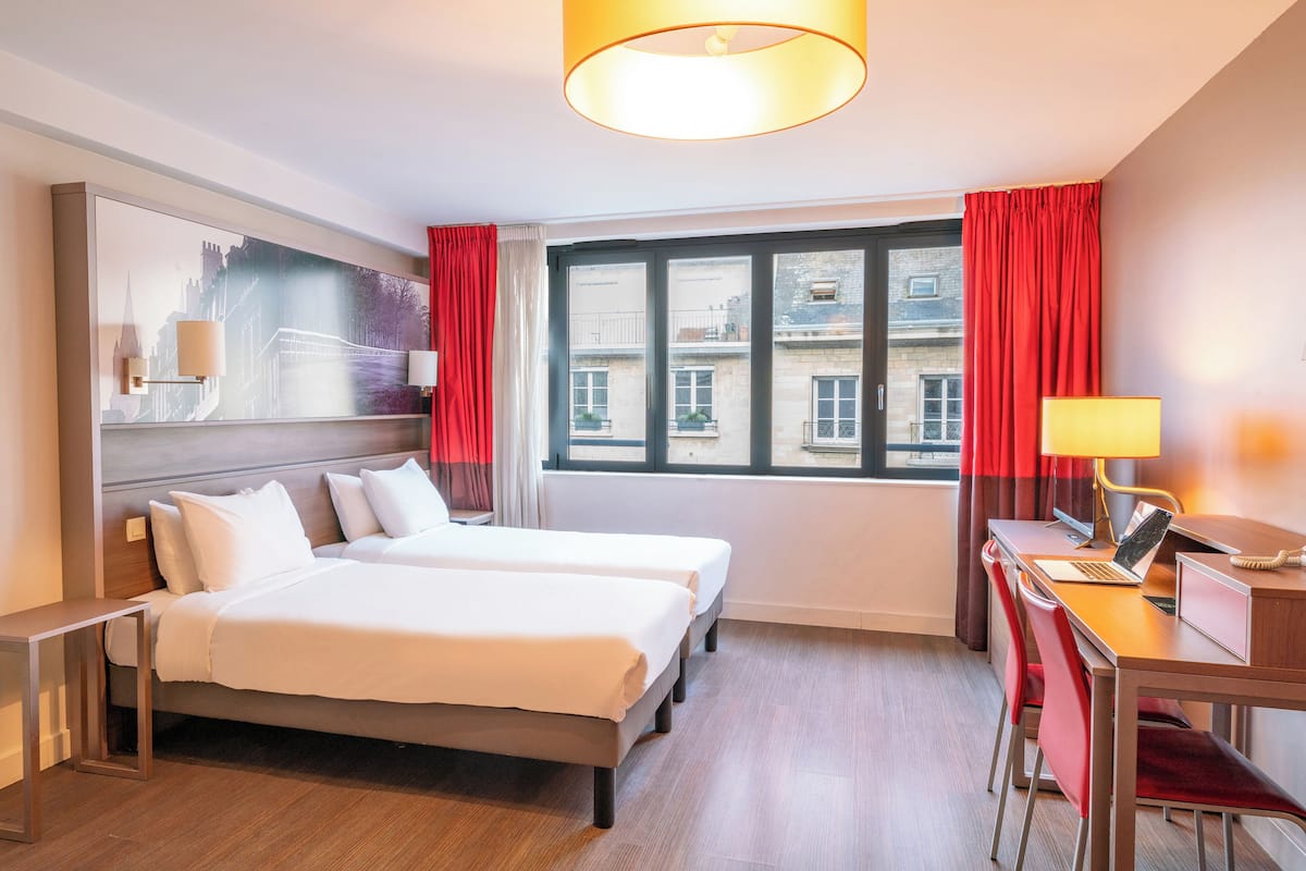 Quarto de hotel com cama, escrivaninha e janela.