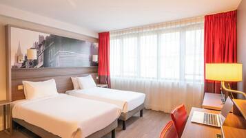 Une chambre d’hôtel avec deux lits, un bureau avec un ordinateur portable, une lampe et un grand tableau représentant un paysage urbain accroché au mur.