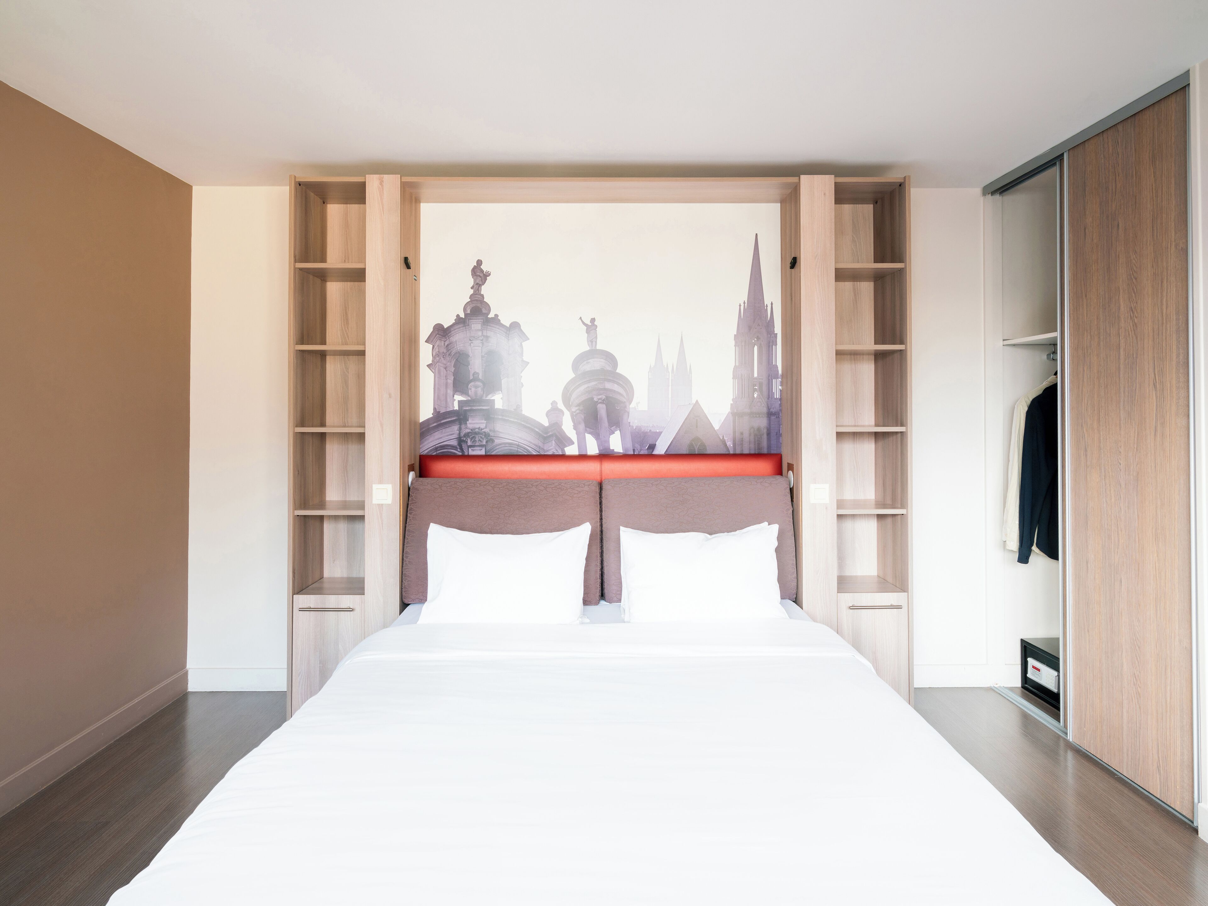 A bedroom with a bed, a cityscape mural on the headboard, wooden shelving, and a wardrobe.