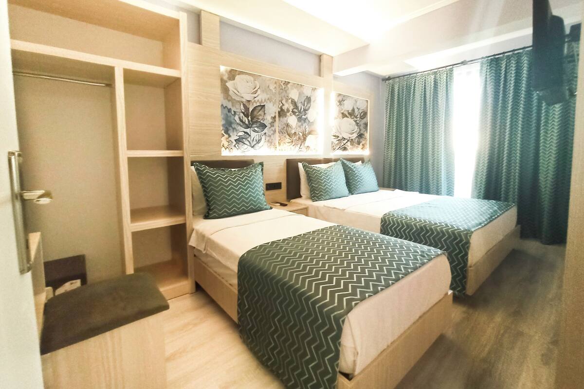 A hotel room with two beds, a wardrobe, and a painting on the wall.