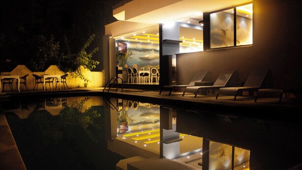 A nighttime view of a pool area with lounge chairs and a restaurant with a mural. - Livaneli Boutique Otel (Alanya)