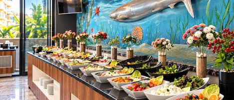 A buffet with various food items and decorative flowers.