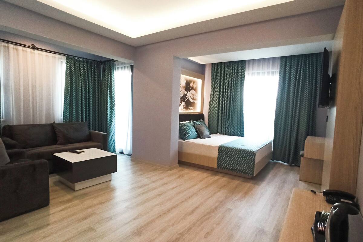 A modern hotel room with a sofa, a small table, a bed with a view, and a desk with a phone.