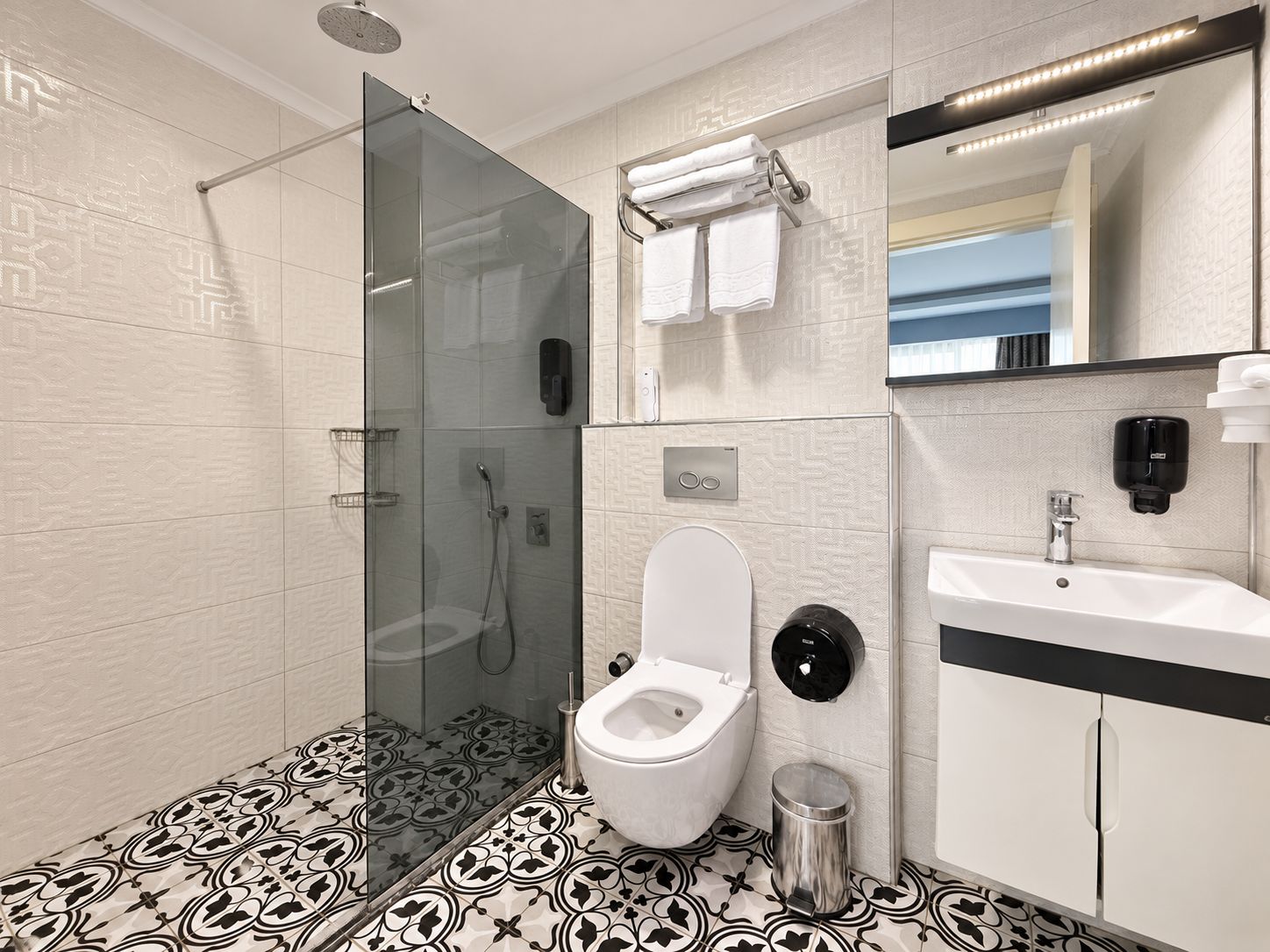 Un baño moderno con ducha de vidrio, inodoro, lavamanos y espejo.