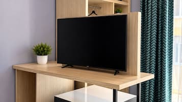 Una habitación moderna con un escritorio de madera, un televisor de pantalla plana, una planta pequeña y una ventana con cortinas.