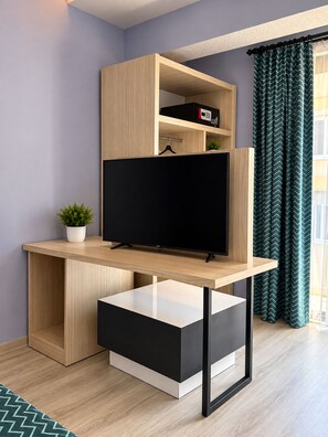 A modern room with a wooden desk, a flat-screen TV, a small plant, and a window with curtains. - Livaneli Boutique Otel (Alanya)