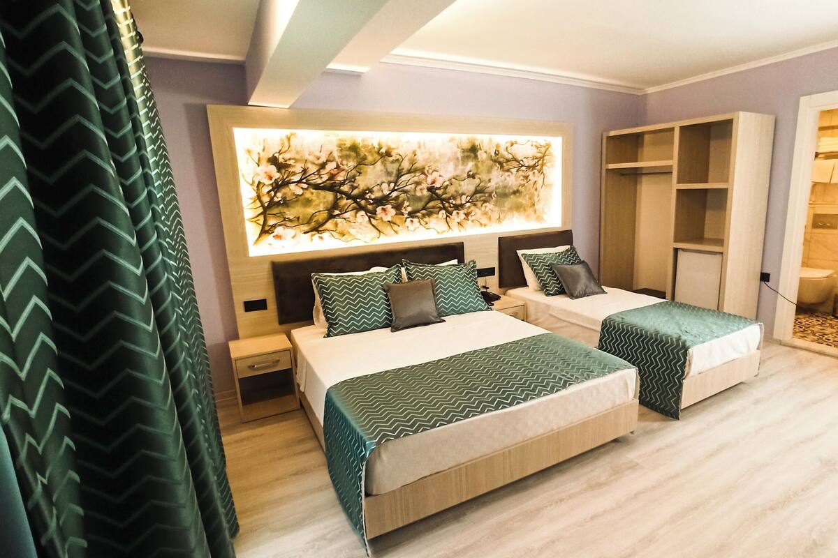 A hotel room with two beds, a large artwork on the wall, a wardrobe, and a bathroom visible through an open door.