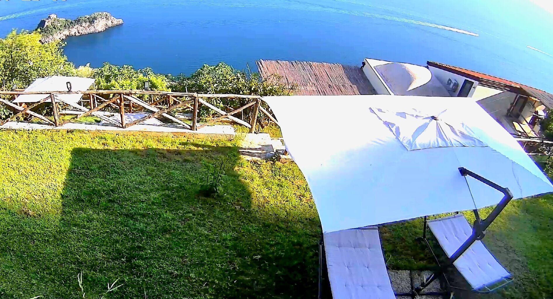 Una terraza en la azotea con un toldo blanco, cubierta de madera y vistas al mar.