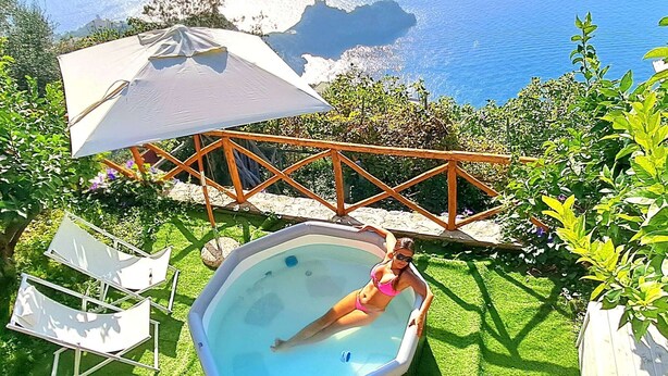 Ein Whirlpool in einem Garten mit Meerblick, umgeben von Grünpflanzen und einer Holzterrasse.