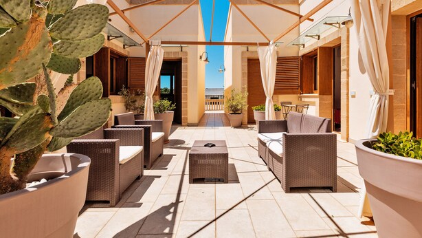 Um terraço ao ar livre com mobiliário de vime, um guarda-sol grande e plantas em vasos.