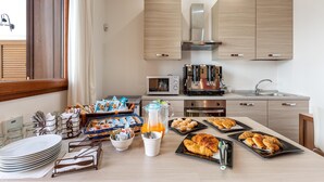 A modern kitchen with wooden cabinets, a stainless steel range hood, a microwave, and a coffee machine. There is a breakfast buffet with plates, bowls, and pastries on the counter. - 2059 Lido Marini Rooms -Tripla (Salve)