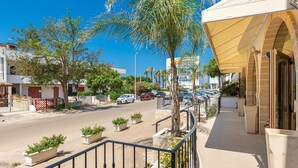 A street view with a building featuring a covered outdoor seating area, potted plants, and parked cars. - 2059 Lido Marini Rooms -Tripla (Salve)