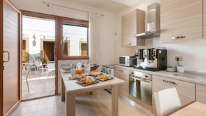 A modern kitchen with stainless steel appliances, a dining area with a table set for breakfast, and a sliding glass door leading to an outdoor patio. - 2059 Lido Marini Rooms -Tripla (Salve)