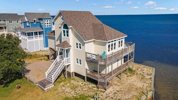 Une propriété située en bord de mer, avec une grande maison dotée d’un balcon et d’un escalier menant à une terrasse.
