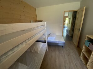 Une petite pièce compacte, dotée d’un lit superposé et d’un lit simple. Les murs et le sol de la pièce sont en bois. Une porte donne accès à une autre pièce.