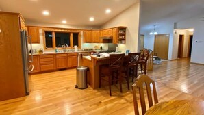 A spacious kitchen with wooden cabinets, a central island with bar stools, and a stainless steel refrigerator. - Sleeps 15 Beautiful Home on 1.2 Acre lot Minutes from Lakes, boat dock & beach (Albert Lea)