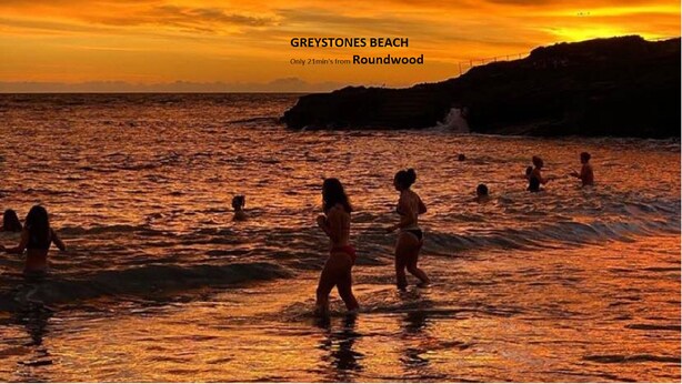 Un coucher de soleil sur la plage de Greystones, avec des gens dans l’eau.