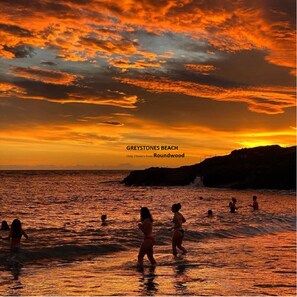 A sunset at Greystones Beach with people in the water.