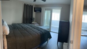 A bedroom with a bed, a fan, a dresser, and a sliding glass door leading to a balcony.