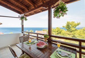 Ein Holztisch mit Blick aufs Meer, eine hängende Blumenkomposition und eine Wassermelone auf dem Tisch.