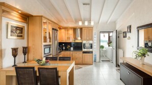 A modern kitchen with wooden cabinets, a central island, and a dining area. - Beautiful and Modern Apartment in Neos Marmaras (Sithonia)