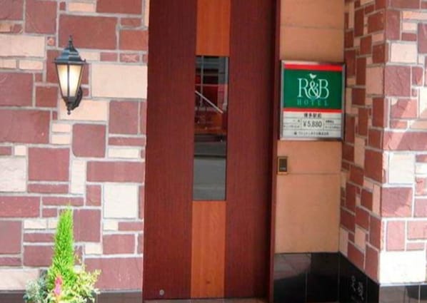 A hotel entrance with a brick facade, a wooden door, and a sign for R&B Hotel.