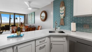 A modern kitchen with a large island, white cabinetry, a blue backsplash, and a view of palm trees.