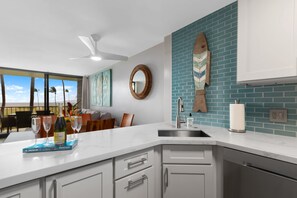 A modern kitchen with a large island, white cabinetry, a blue backsplash, and a view of palm trees.