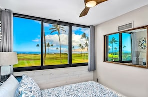 A bedroom with a large window offering a view of a golf course and palm trees.