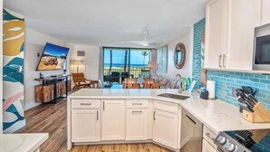 A modern kitchen with white cabinets, a black stove, and a large window overlooking a balcony.