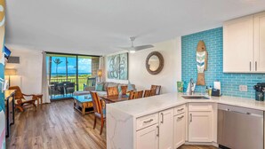 A modern kitchen with white cabinets, a marble countertop, and a view of the ocean through large windows.