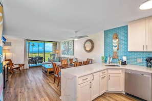 A modern kitchen with white cabinets, a marble countertop, and a view of the ocean through large windows.