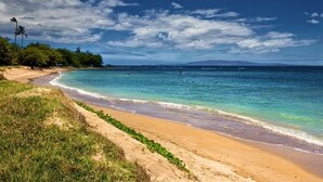 A beach with clear turquoise waters, a sandy shore, and a distant mountain range.