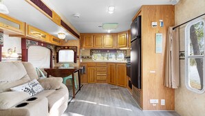 Eine kompakte Küchenzeile für ein Wohnmobil mit Holzausstattung, einem Kühlschrank und einer Essecke mit Tisch und Stühlen.