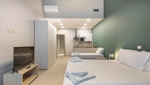 A modern hotel room with a large bed, a TV on a stand, a kitchenette, and a bathroom. - Camplus Regio Parco (Turin)