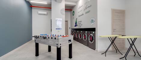 A clean, modern room with a foosball table, a washing machine area, and a table with a yellow top.
