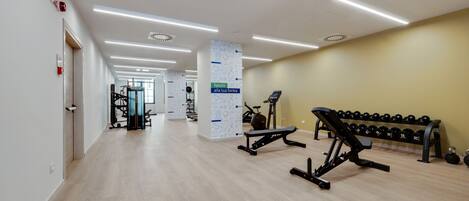 A modern gym with exercise equipment, a bench, and dumbbells.