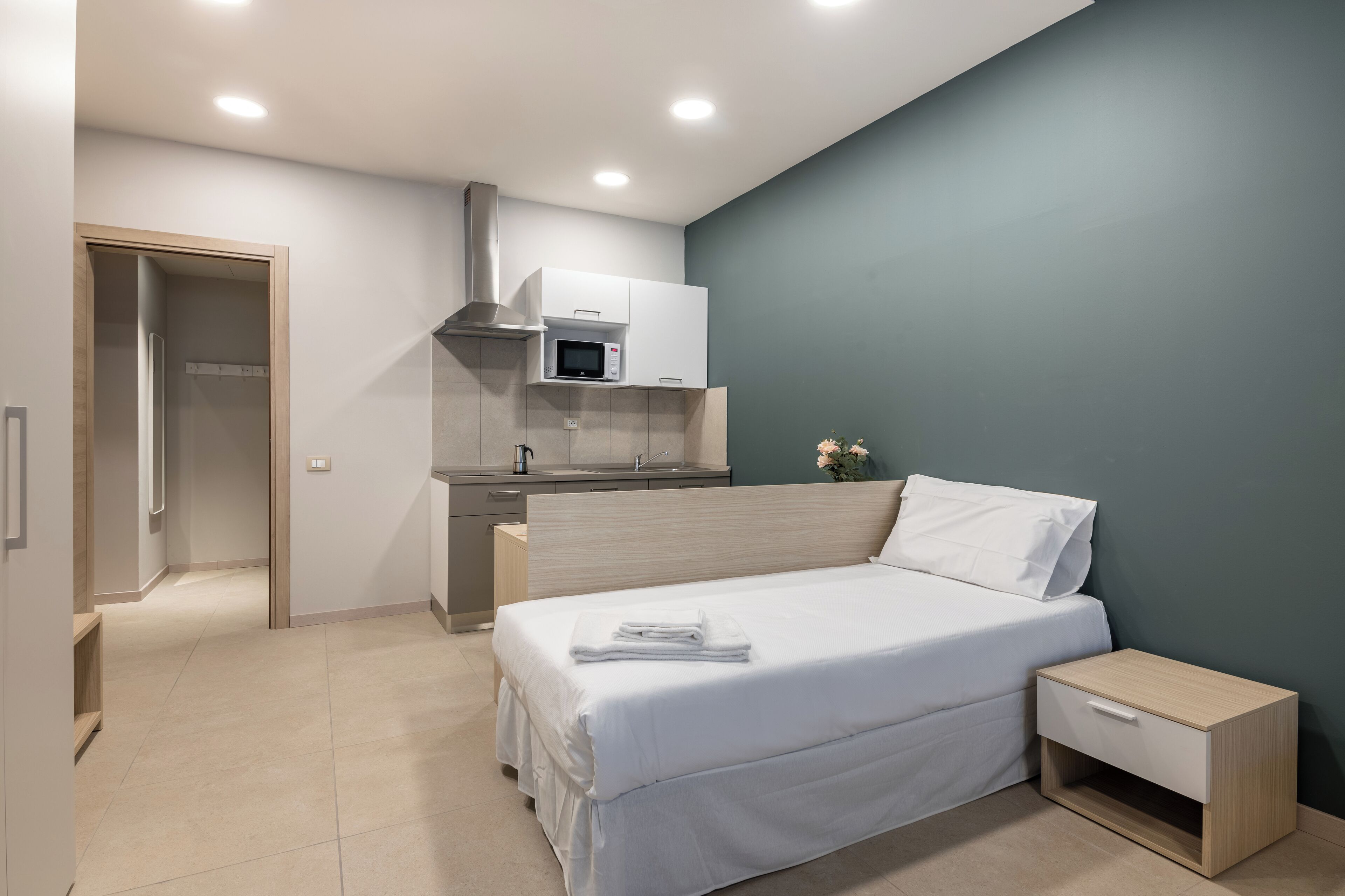Ein modernes Schlafzimmer mit Bett, Nachttisch und einer integrierten Küchenzeile.