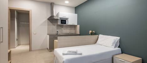 Quarto moderno com cama, mesa de cabeceira e cozinha compacta.