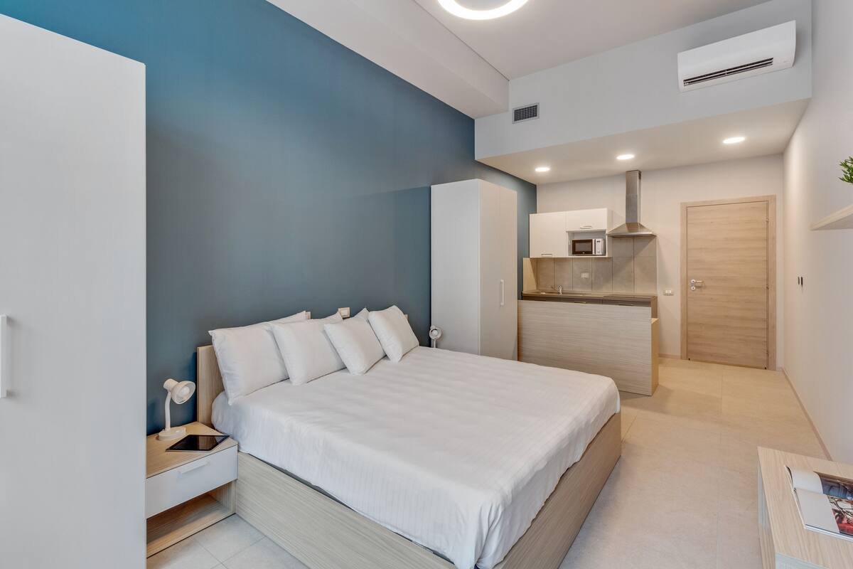 A modern bedroom with a bed, bedside table, and a built-in kitchenette.