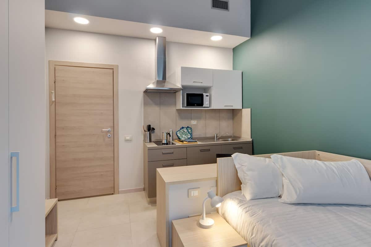 A compact bedroom with a bed, bedside table, and a small desk area with a lamp.
