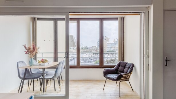 Zona pranzo moderna con tavolo e sedie, un vaso decorativo e vista sulla città attraverso ampie finestre.