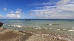Paesaggio costiero con una passeggiata in cemento, mare calmo e un molo in lontananza.