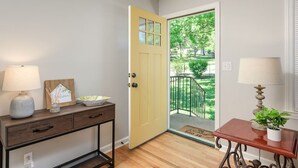A wooden door with a glass panel, a welcome mat, a small table with a lamp, and a potted plant. - Yellow Door Cottage - 3BR, Pet & family friendly! (Chattanooga)