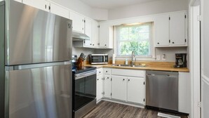 A modern kitchen with stainless steel appliances, white cabinetry, and a window with blinds. - Yellow Door Cottage - 3BR, Pet & family friendly! (Chattanooga)
