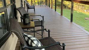 Terraza techada al aire libre con mobiliario de mimbre y vista a un paisaje verde.