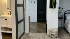 Un dormitorio moderno con techo de madera, una puerta blanca, una planta pequeña y una cesta con la etiqueta 'Misc'.