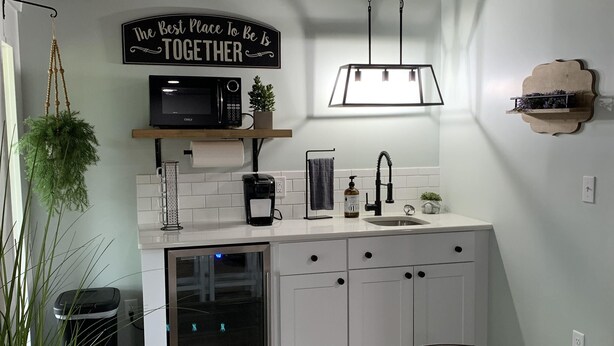 Una cocina moderna con armarios blancos, techo de madera, microondas negro y un cartel que dice 'The Best Place To Be Is Together'.