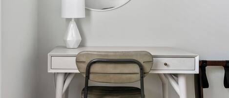 A white desk with a round mirror, a lamp, and a chair in a room with wooden flooring and a patterned rug.